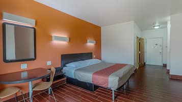 A hotel room with a bed, a table with chairs, a mirror, and a door leading to another room.