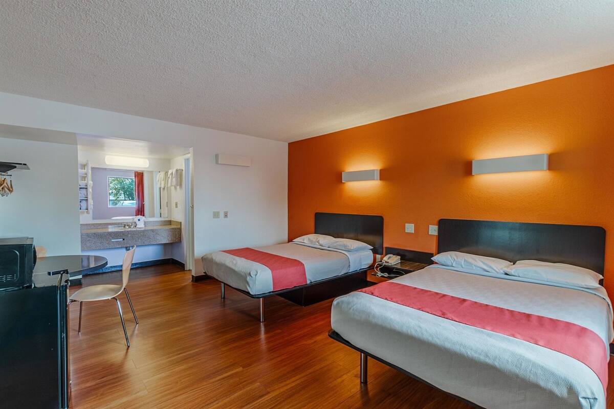 A hotel room with two beds, a desk, and a bathroom visible through an open door.