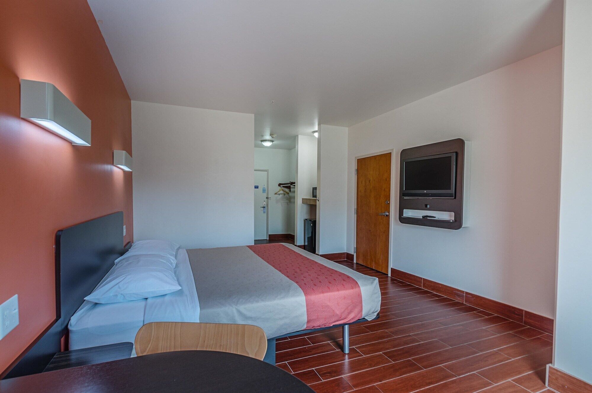 A hotel room with a bed, a TV mounted on the wall, and a wooden floor.
