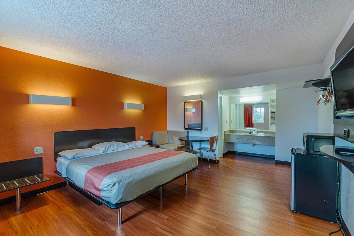 A modern hotel room with a bed, bedside tables, a desk, a mirror, and a TV.