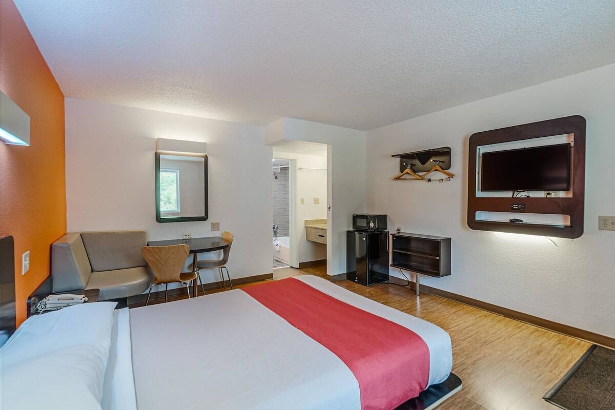 A hotel room with a bed, a desk, a chair, a TV, and a mirror.