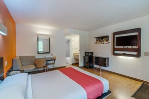 Una habitación de hotel con cama, escritorio, silla, televisor y espejo.