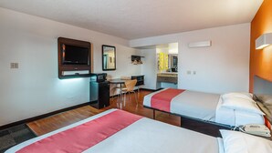 Hotelkamer met twee bedden, een bureau met stoel, een magnetron, een televisie en een badkamer zichtbaar door een geopende deur.