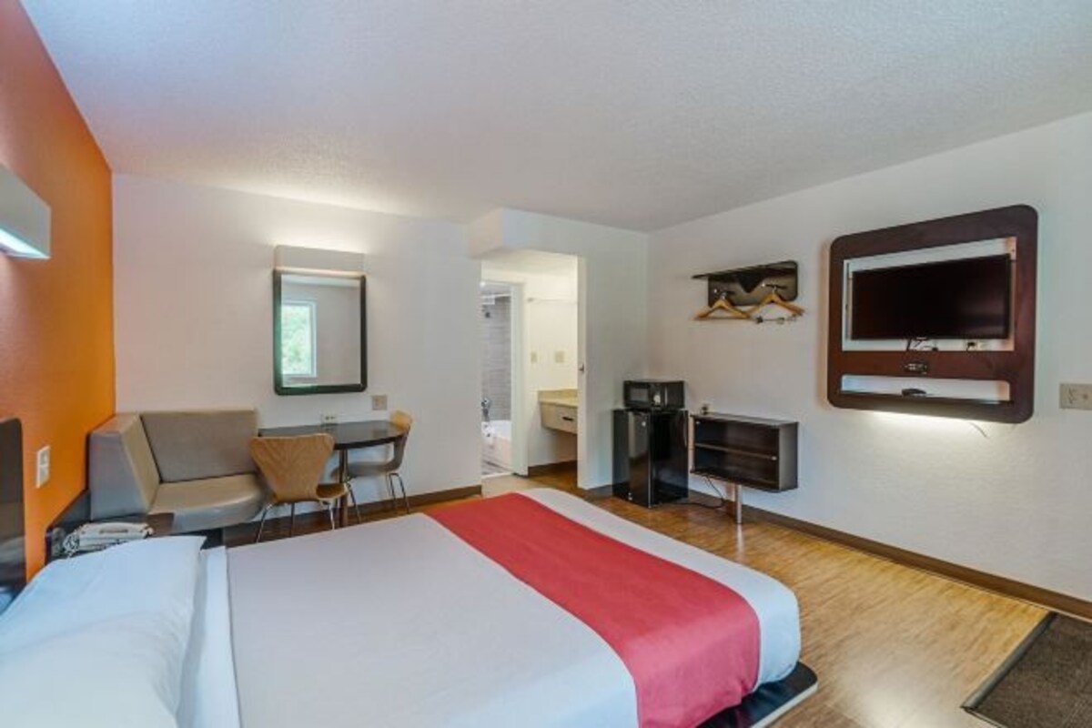 Ett hotellrum med en säng, ett skrivbord, en stol, en tv och en spegel.