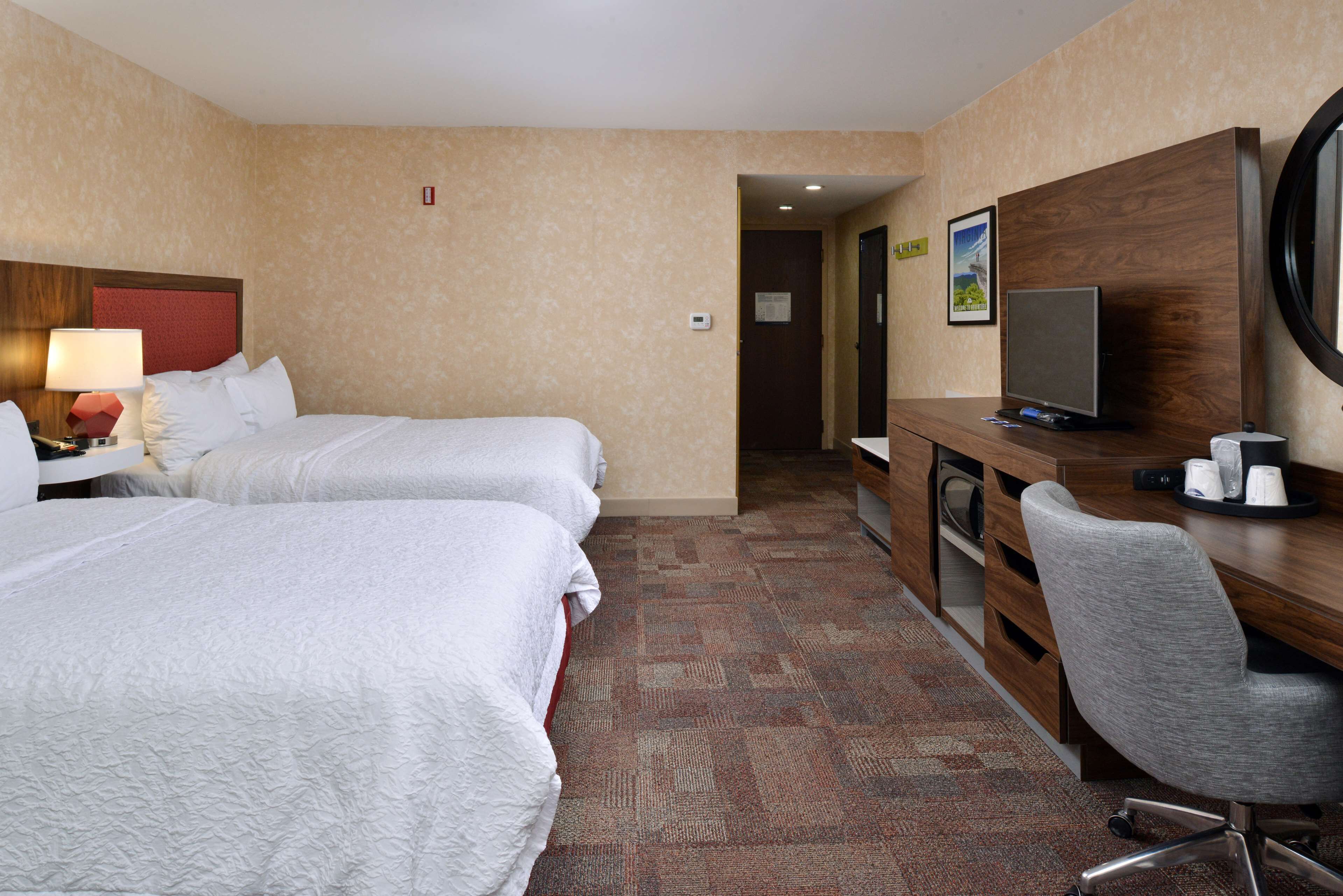 Habitación de hotel con dos camas, un escritorio con silla, televisor y baño visible a través de una puerta abierta.