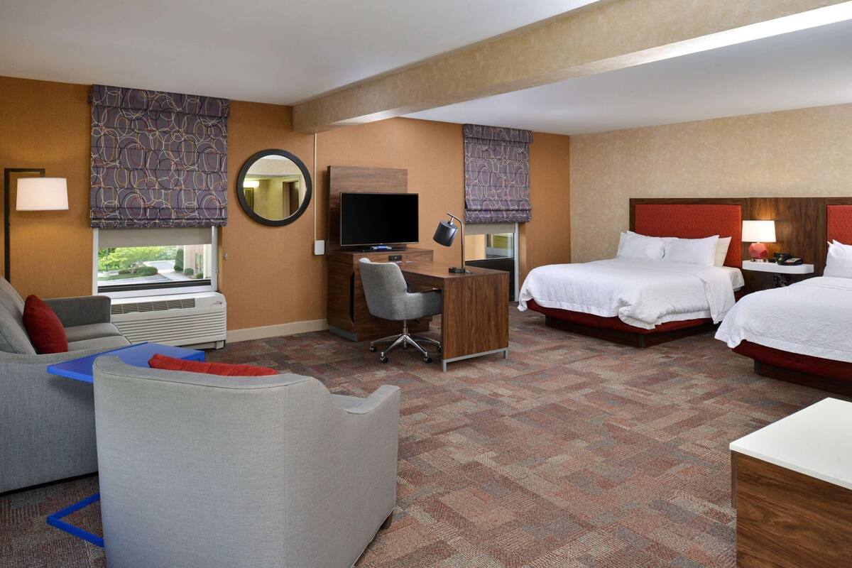 A hotel room with two beds, a desk, a chair, a TV, and a window.