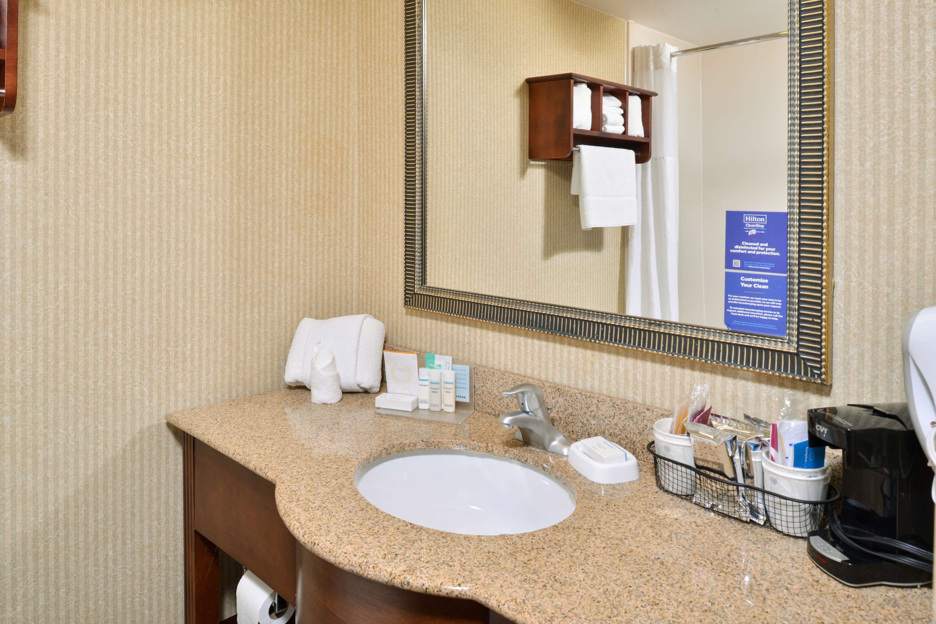 A hotel bathroom with a granite countertop sink, a large mirror, and a towel rack.