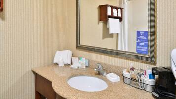 A hotel bathroom with a granite countertop sink, a large mirror, and a towel rack.
