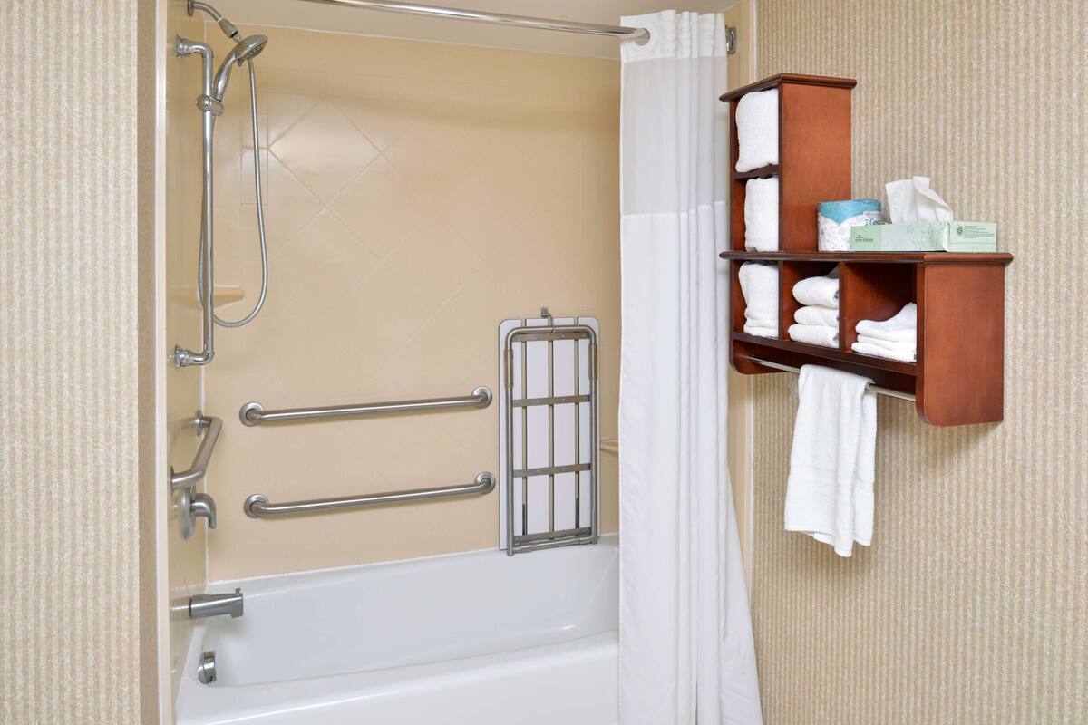 A bathroom with a bathtub, shower, and a towel rack with neatly folded towels.