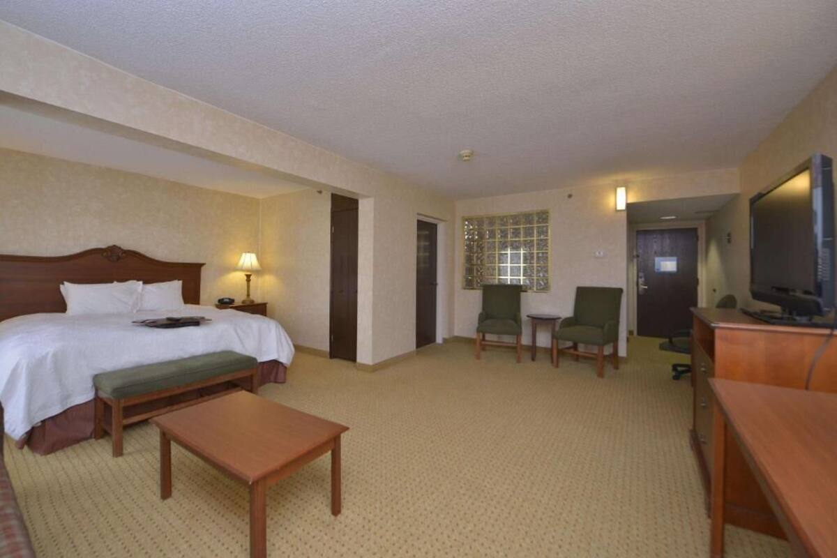 A hotel room with a bed, a desk, a chair, a television, and a window with blinds.