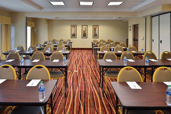 A conference room with multiple tables and chairs, water bottles on each table, and a patterned carpet.