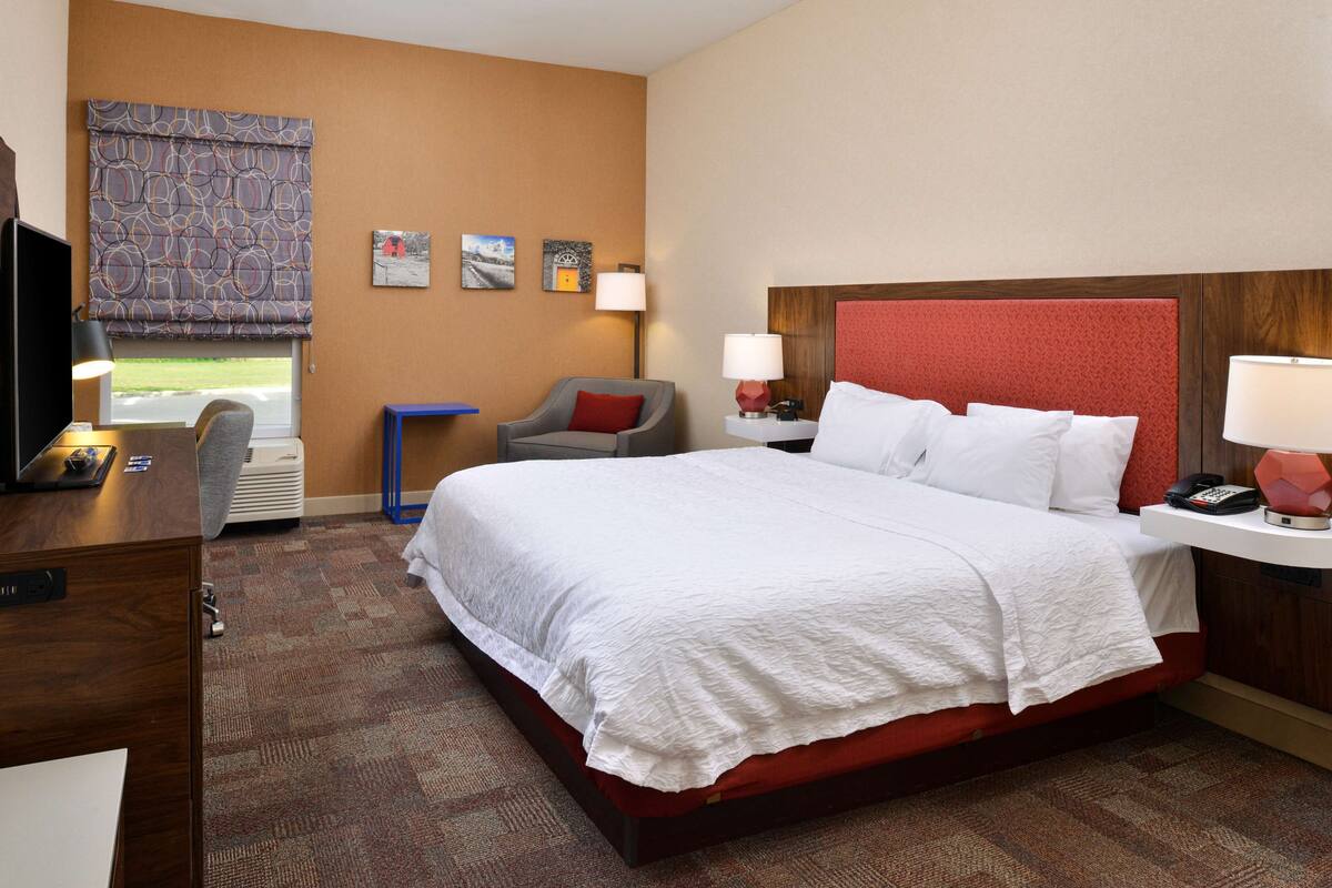 A hotel room with a large bed, a desk, a chair, and a window with a view.