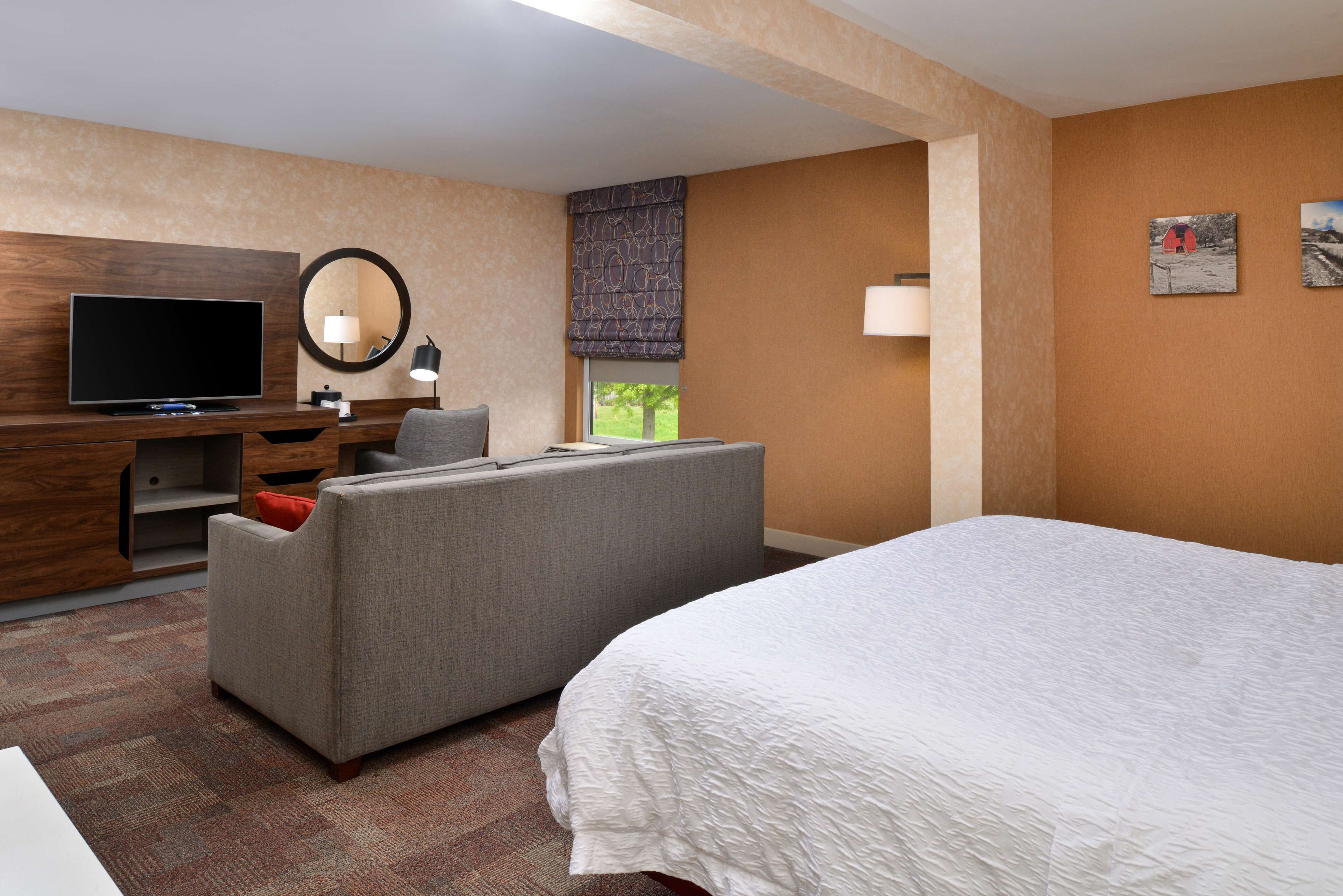 Ein Hotelzimmer mit Bett, Fernseher, Sofa, Schreibtisch und einem Fenster mit Blick.