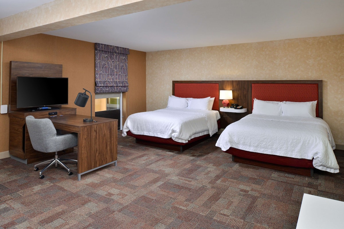 A hotel room with two beds, a desk with a TV, and a chair.