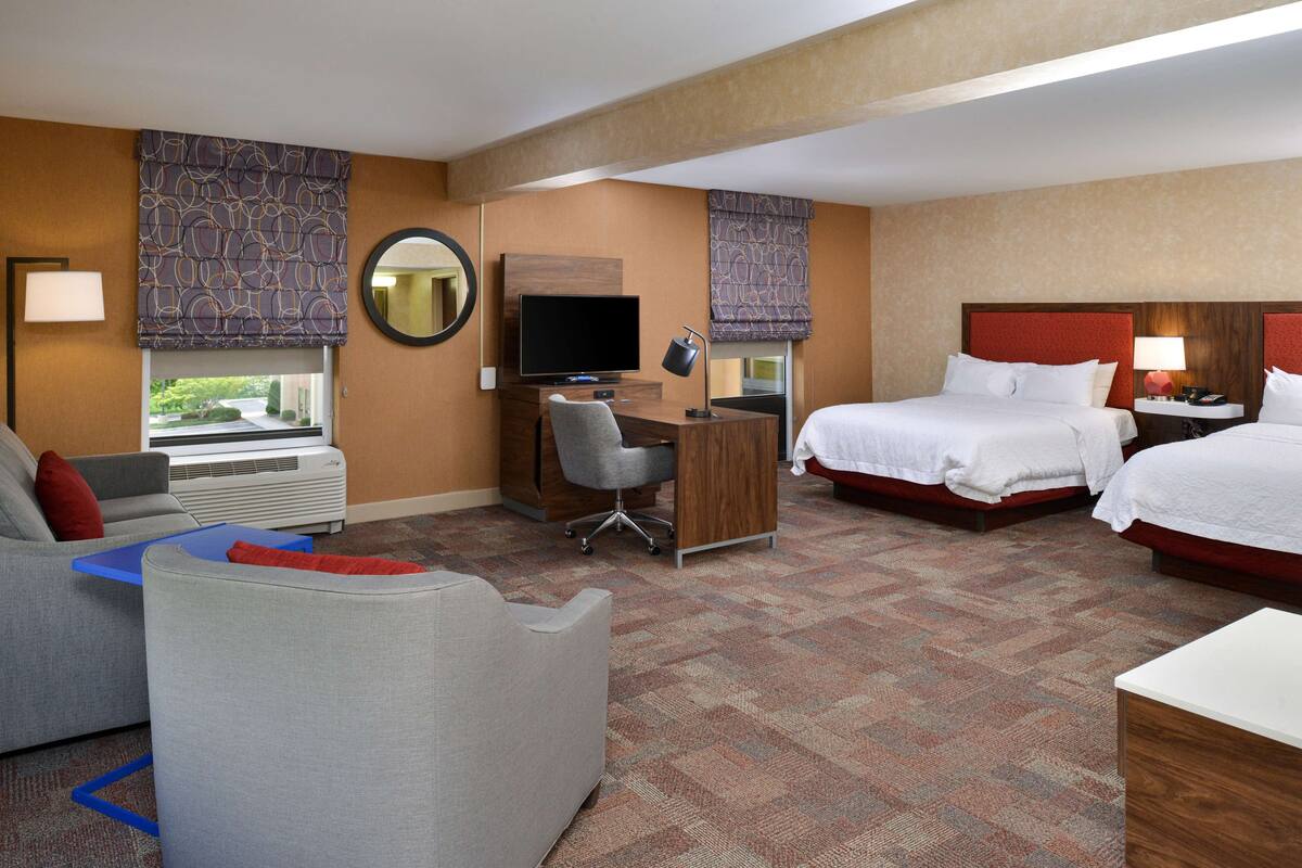 A hotel room with two beds, a desk with a computer, a TV, and a sofa.