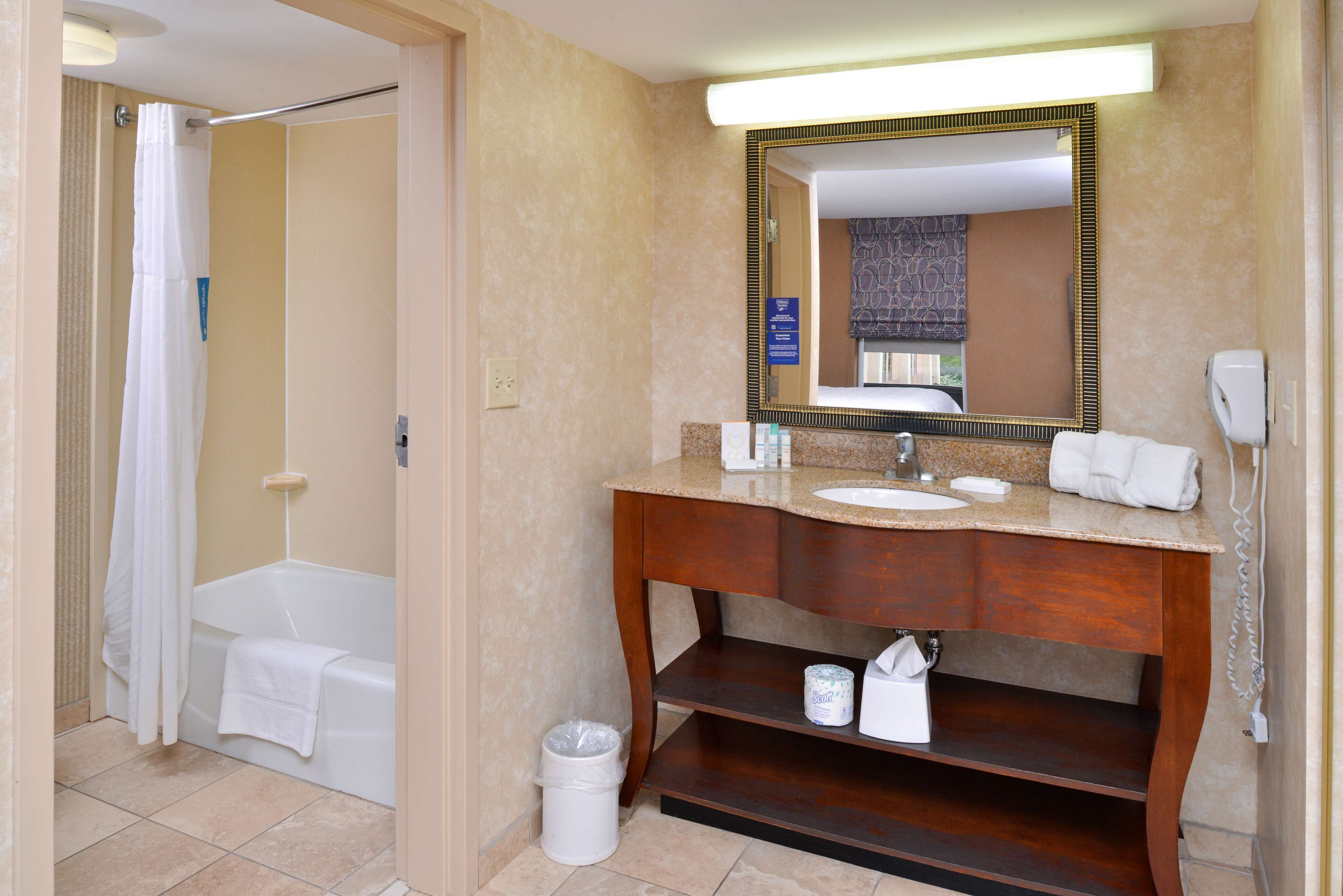 A bathroom with a bathtub, a sink, a vanity with a mirror, and a trash can.