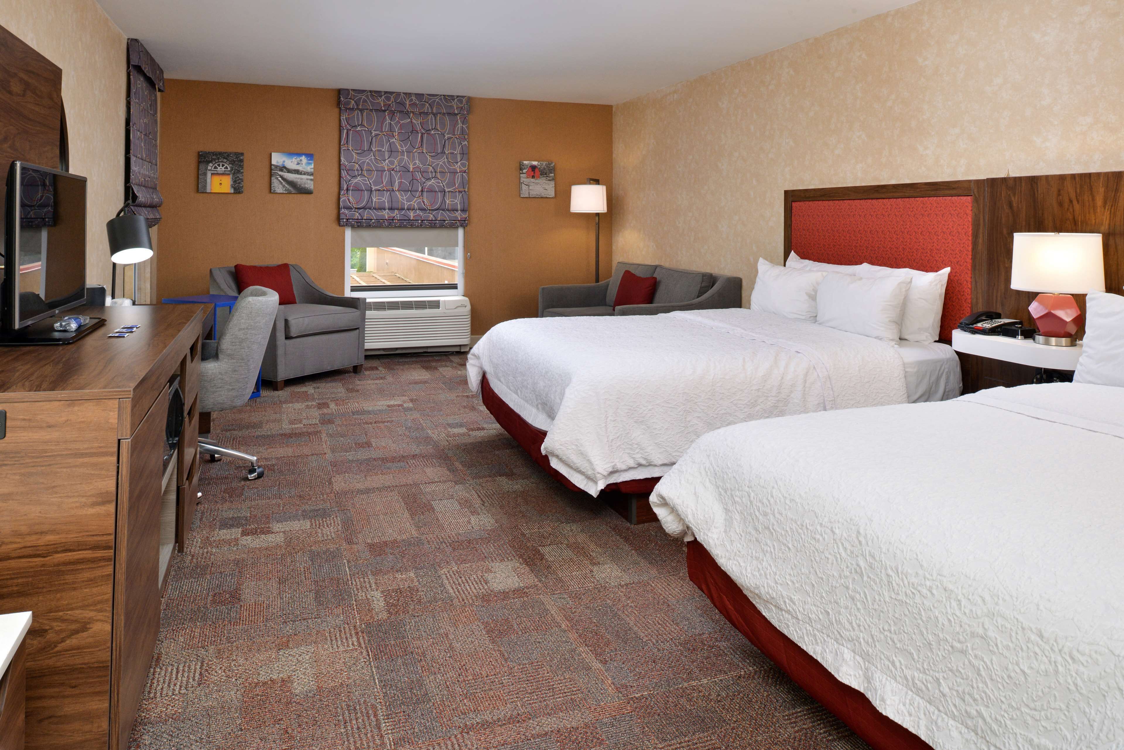 A hotel room with two beds, a desk, a chair, and a TV.