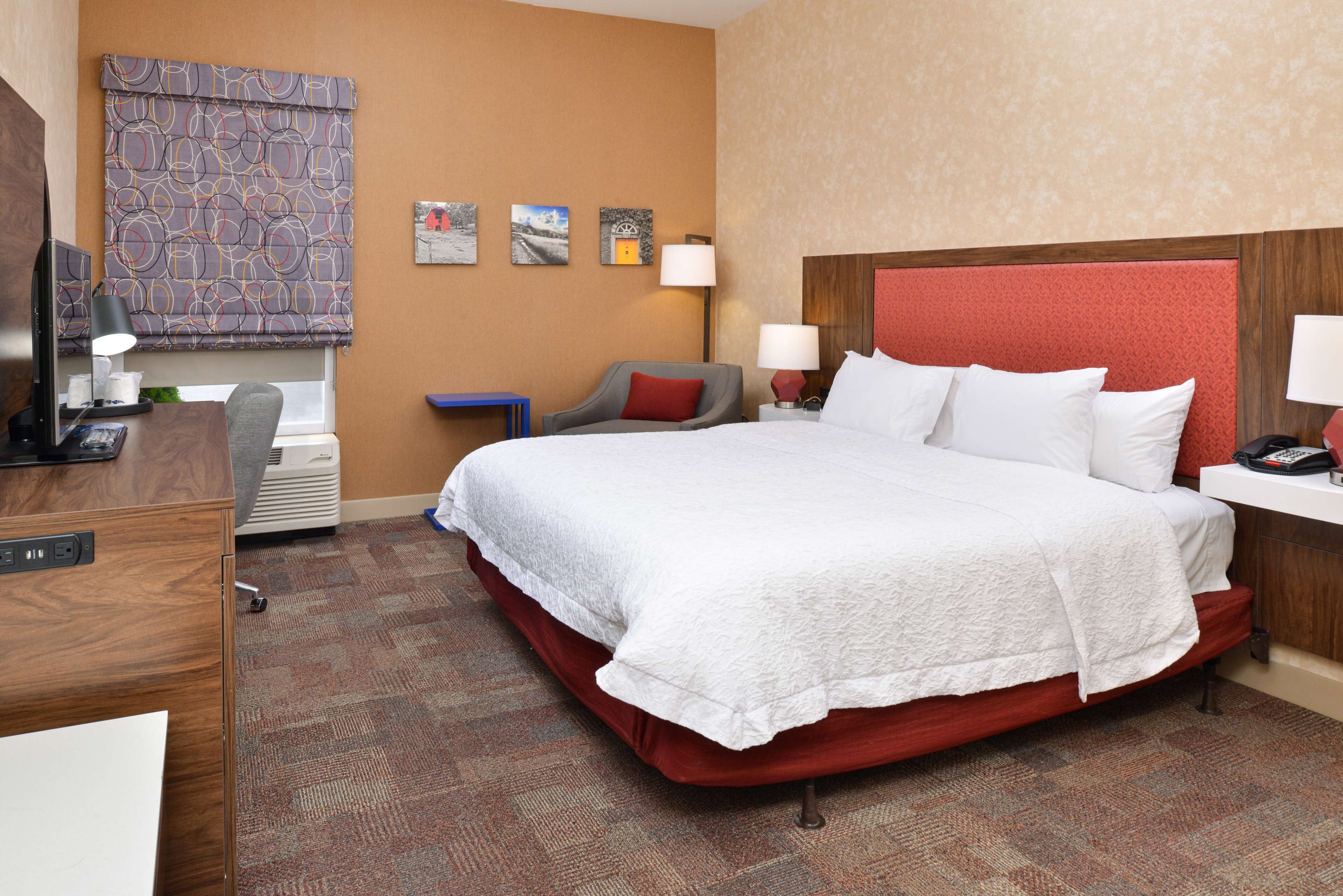 Habitación de hotel con una cama grande, un escritorio con una computadora, una silla y una ventana con cortina estampada.