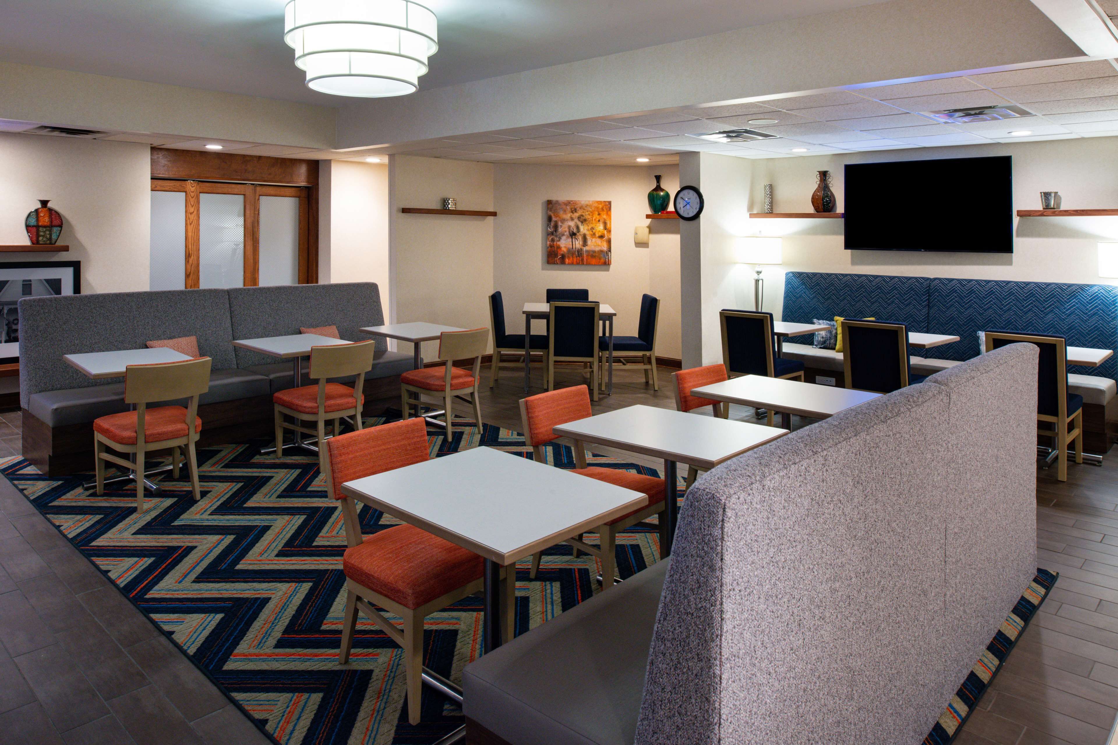 A hotel lobby with seating areas, tables, a TV, and artwork on the walls.
