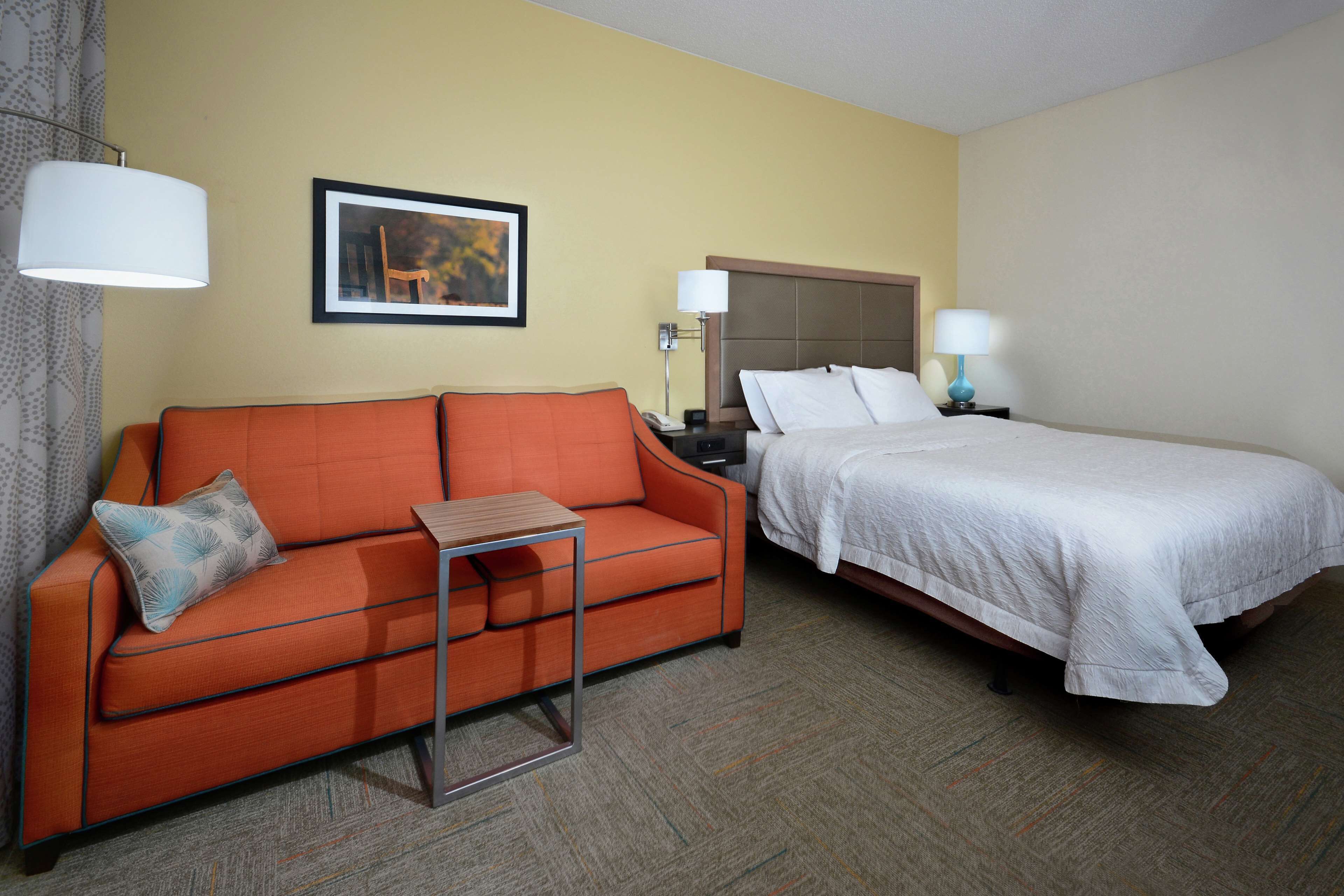 A hotel room with a single bed, a sofa, a small table, and two bedside lamps.