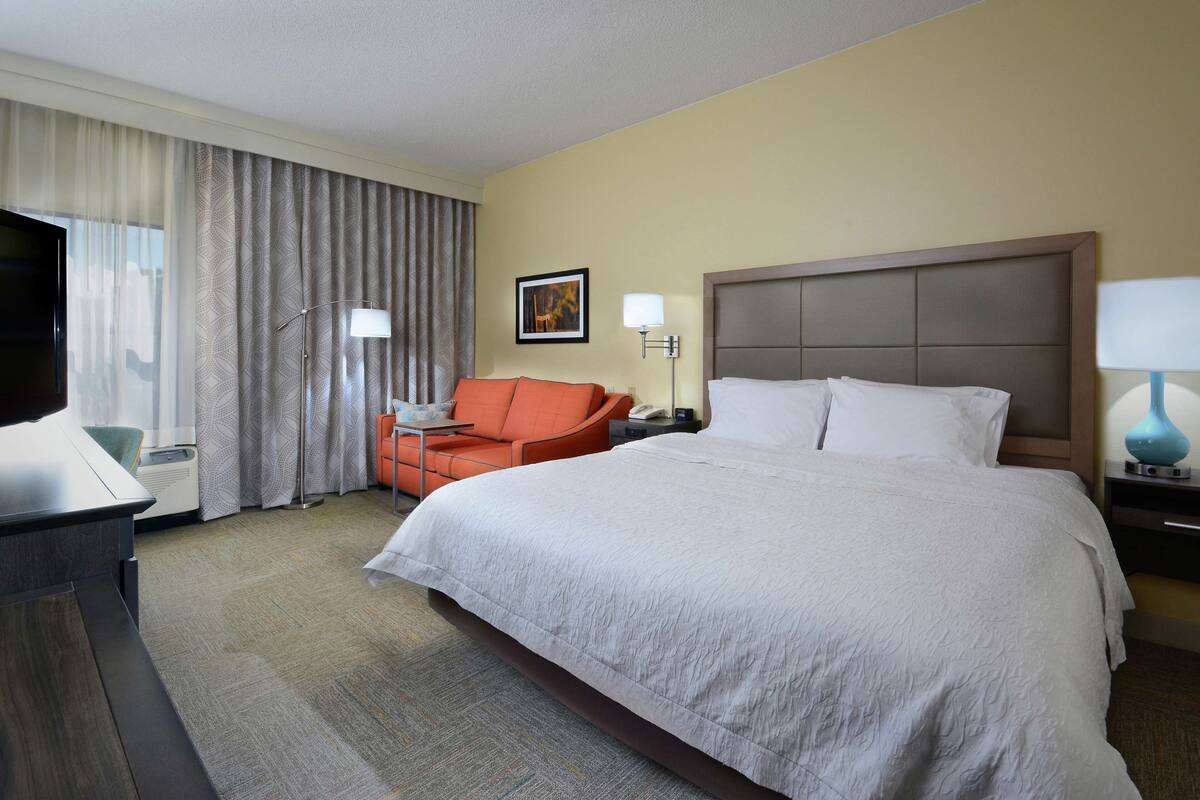 A hotel room with a large bed, a desk, a chair, a television, and a window with curtains.