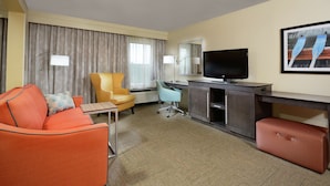 Une chambre d’hôtel équipée d’un canapé, d’un fauteuil, d’un bureau, d’une télévision et d’une grande fenêtre avec des rideaux.