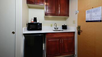 A compact kitchen with wooden cabinets, a microwave, a coffee maker, and a dishwasher.