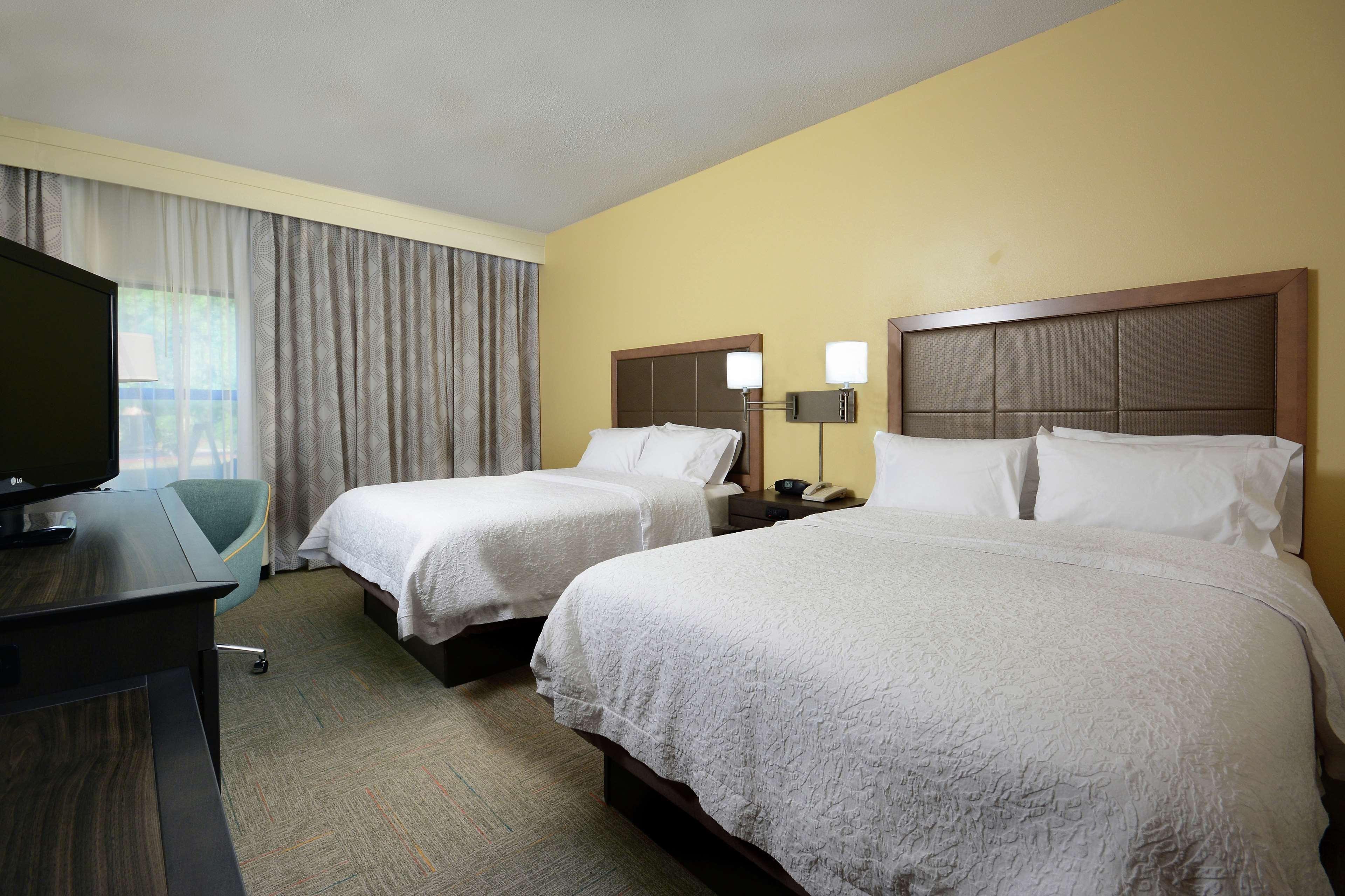 Une chambre d’hôtel avec deux lits, un bureau avec une télévision et une fenêtre avec des rideaux.