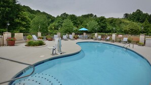 Une piscine entourée d’une clôture et de verdure, avec des chaises longues et des parasols.