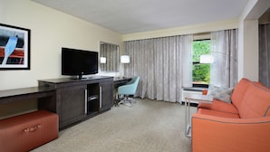 Une chambre d’hôtel équipée d’un téléviseur à écran plat, d’un bureau avec une chaise, d’un canapé et d’une fenêtre avec des rideaux.