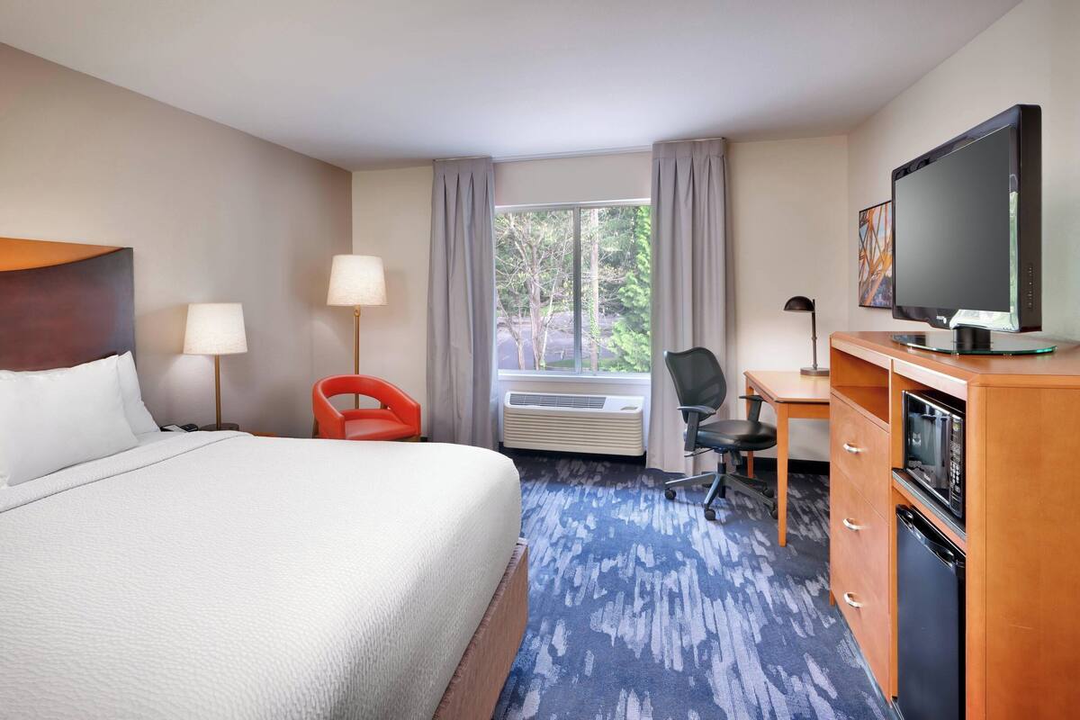 A hotel room with a large bed, a desk, a television, and a microwave.
