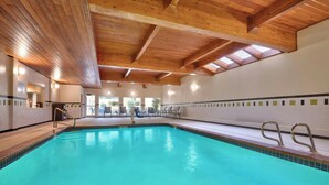 Una piscina interior con vigas de madera y tragaluces, rodeada de paredes y suelo de baldosas.