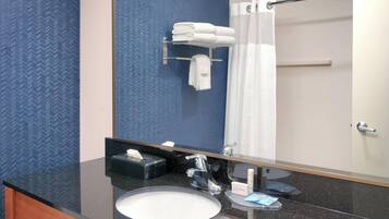 A bathroom with a black granite countertop, a white sink, a mirror, a towel rack with folded towels, and a shower curtain.