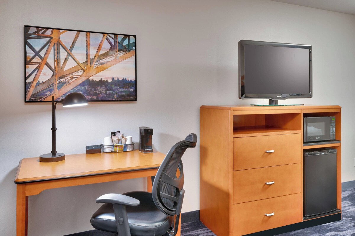 Een hotelkamer met een houten bureau, een zwarte bureaustoel, een flatscreen televisie, een magnetron en een koelkast.