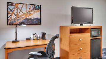Une chambre d’hôtel équipée d’un bureau en bois, d’un fauteuil de bureau noir, d’un téléviseur à écran plat, d’un four à micro-ondes et d’un réfrigérateur.