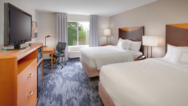 Habitación de hotel con dos camas, un escritorio, televisión y ventana con cortinas.