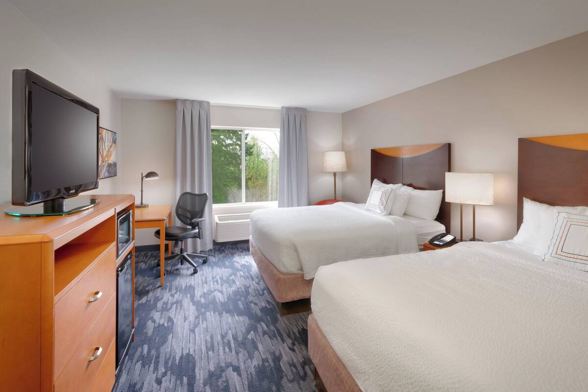 A hotel room with two beds, a desk, a television, and a window with curtains.