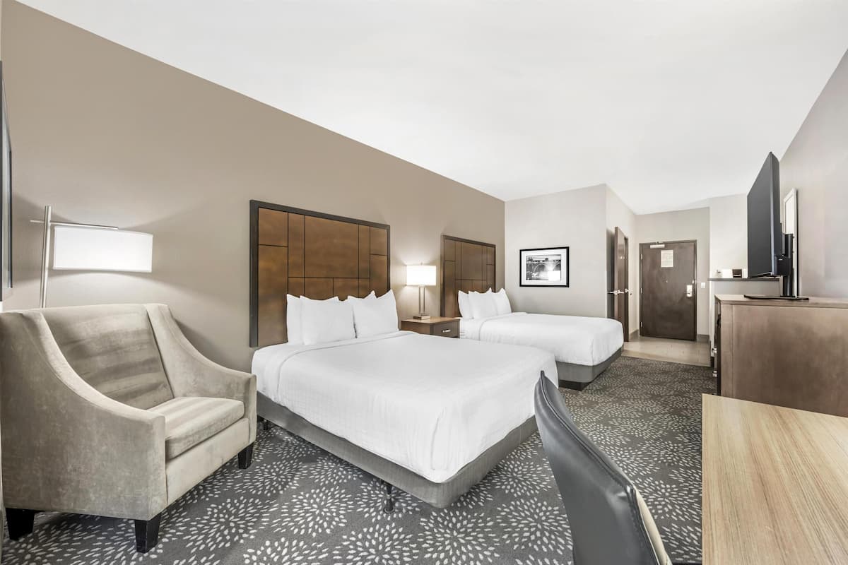 A hotel room with two beds, a sofa, a desk, a TV, and a door.