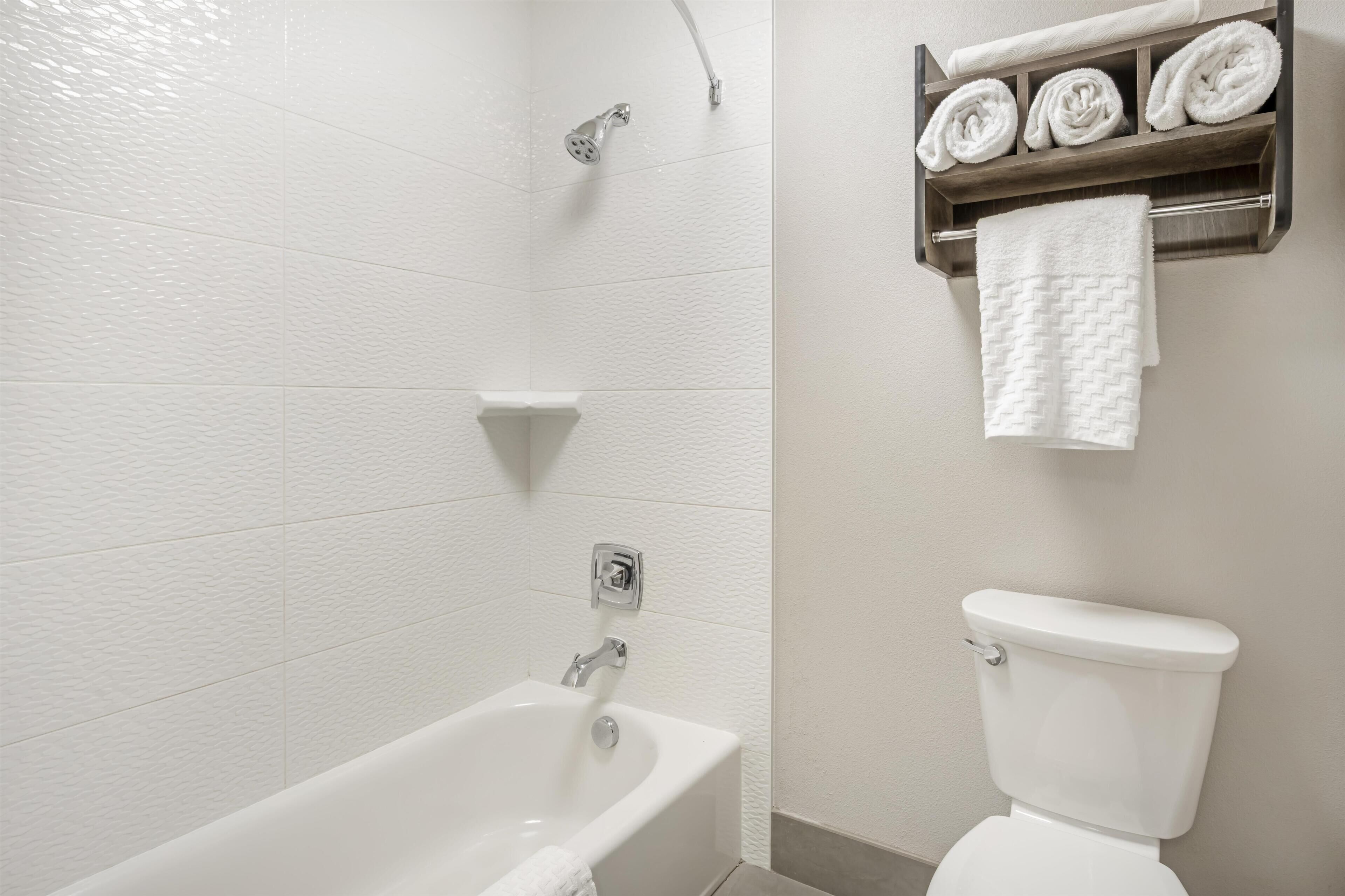 A bathroom with a white bathtub, a toilet, and a towel rack with towels.
