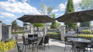 An outdoor patio with tables and chairs, two large umbrellas, and a grill.