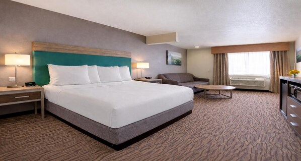 A hotel room with a large bed, a desk, a chair, a small table, and a window with curtains. - Best Western Plus Peppertree Airport Inn (Spokane)