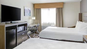 A hotel room with a flat-screen TV, a desk with a chair, two beds, and a large window with curtains.