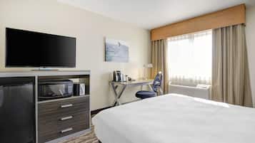 A hotel room with a bed, a desk with a computer, a flat-screen TV, a microwave, and a refrigerator.