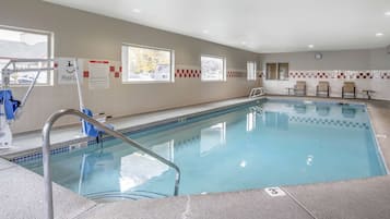 An indoor swimming pool with clear water, a lifeguard chair, and a pool ladder.