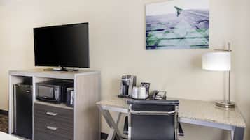 A hotel room with a flat-screen TV, a microwave, a coffee maker, a desk, and a chair.