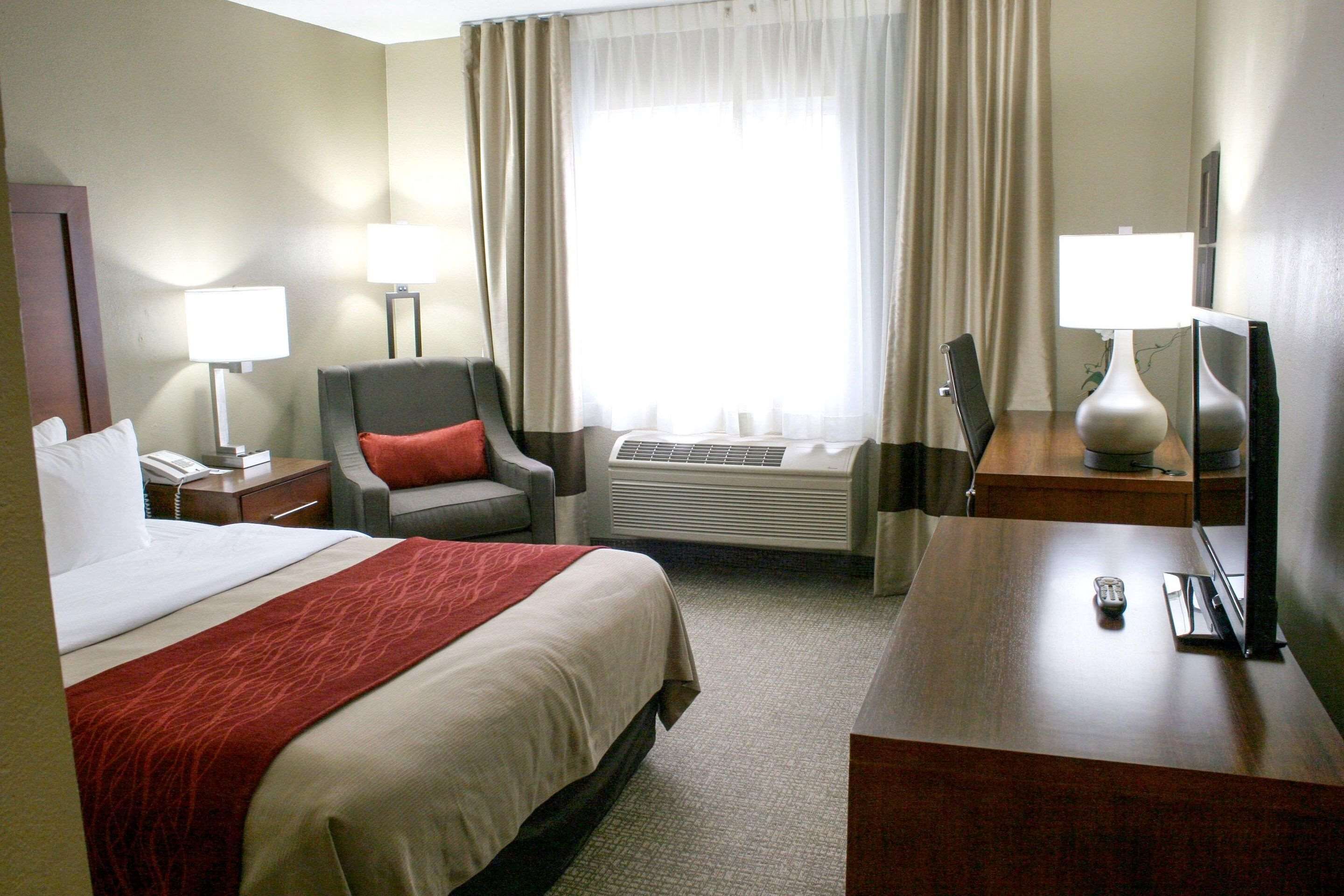 Une chambre d’hôtel équipée d’un lit, d’un bureau, d’une chaise, d’une télévision, d’une lampe et d’une fenêtre avec des rideaux.