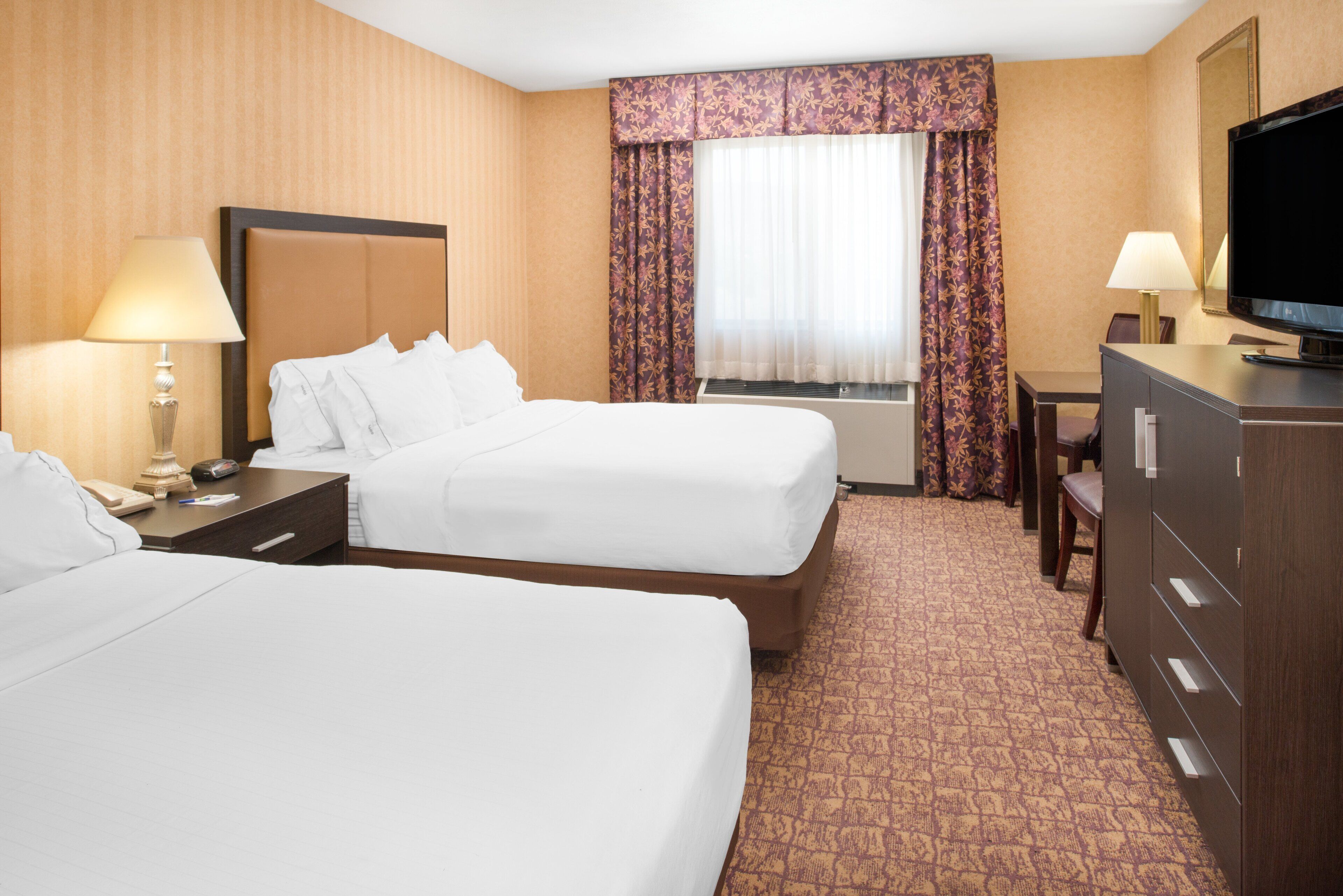 A hotel room with two beds, a desk, a television, and a dresser.