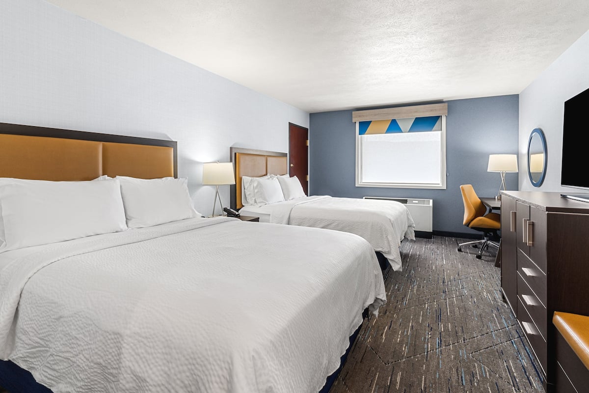 A hotel room with two beds, a desk, a chair, a TV, and a dresser.