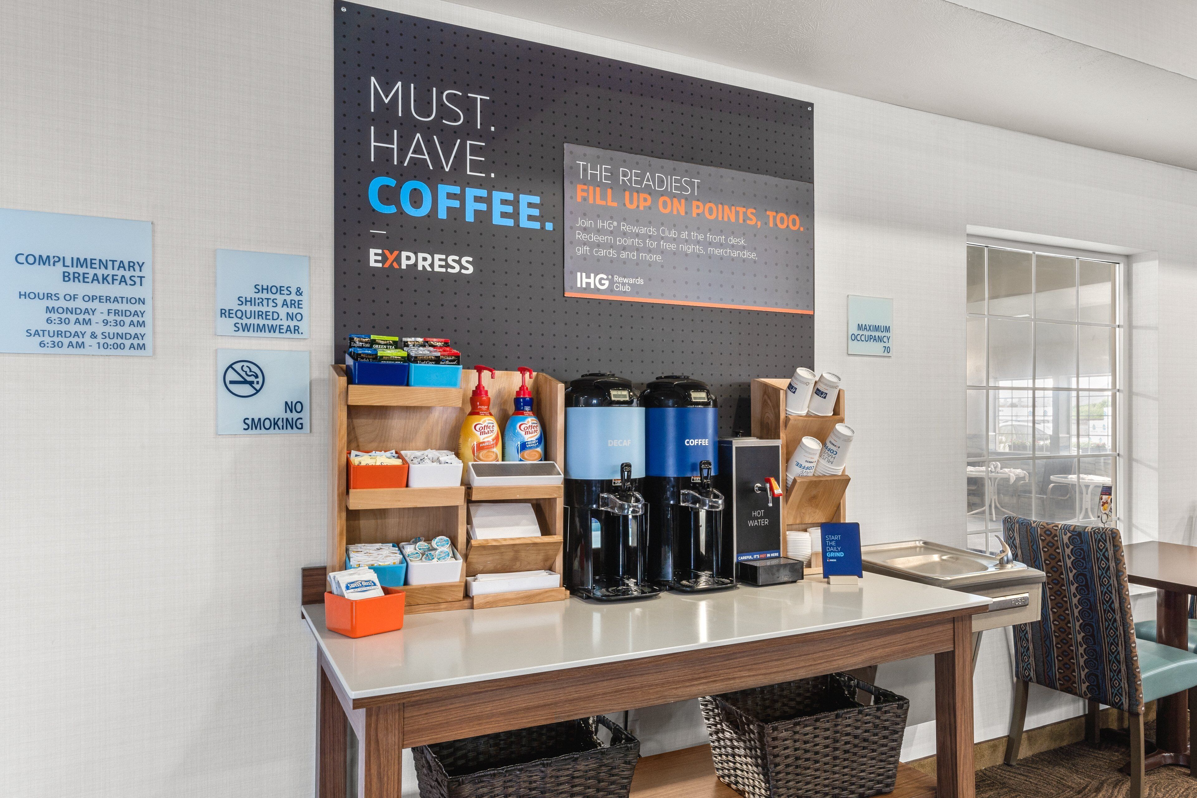 Un espace dédié au café, agrémenté d’une affiche faisant la promotion du programme de fidélité IHG Rewards Club et d’une autre indiquant les heures du petit-déjeuner offert.