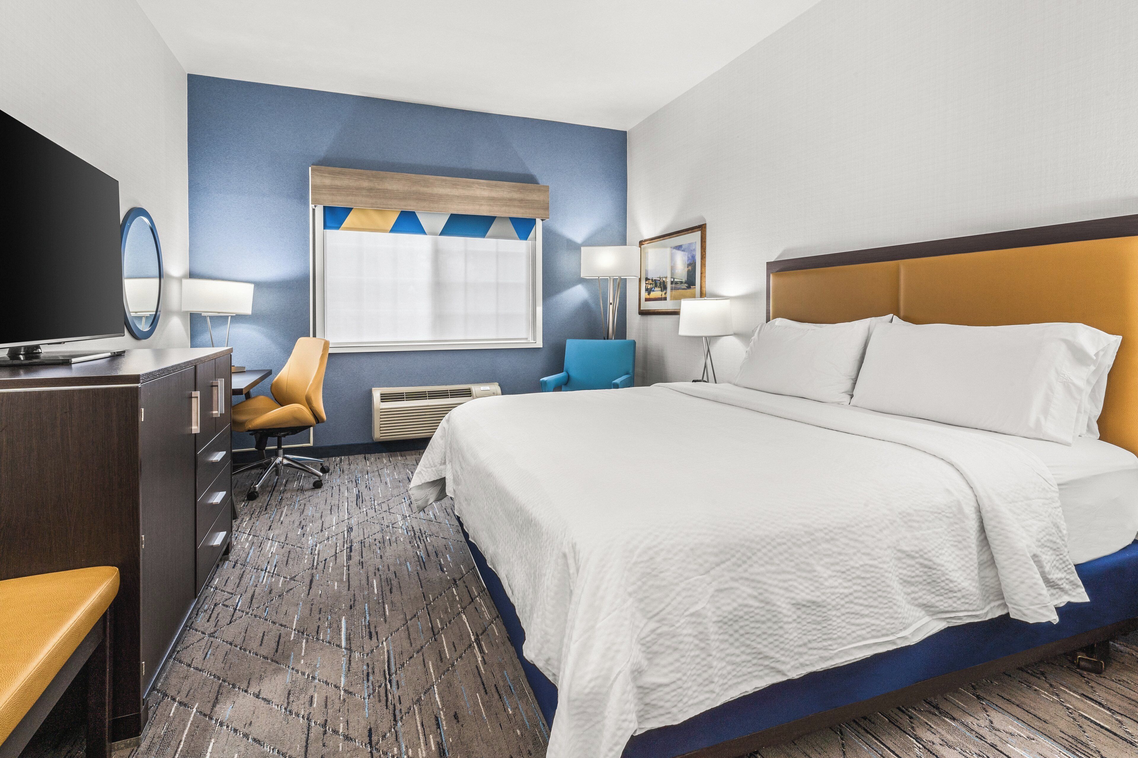 A hotel room with a bed, a desk, a chair, a television, and a window.